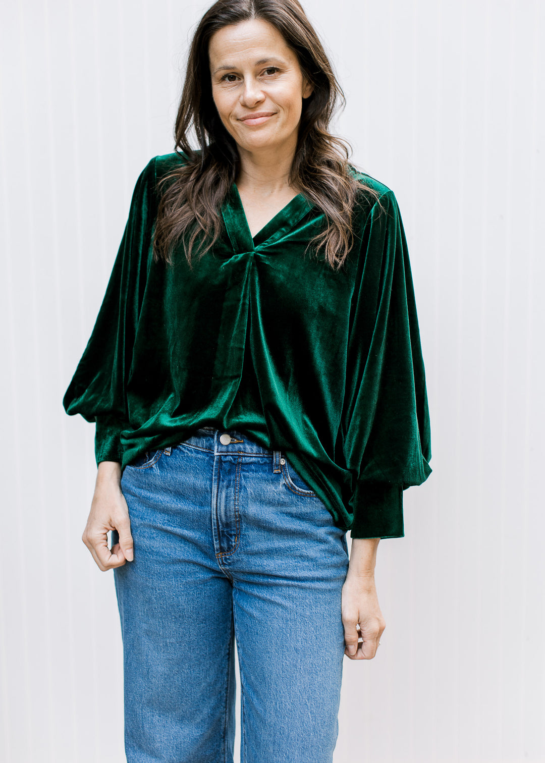 Front view of bottle green velvet blouse with gathered V-neckline and cuffed bubble sleeves, tucked into blue jeans.