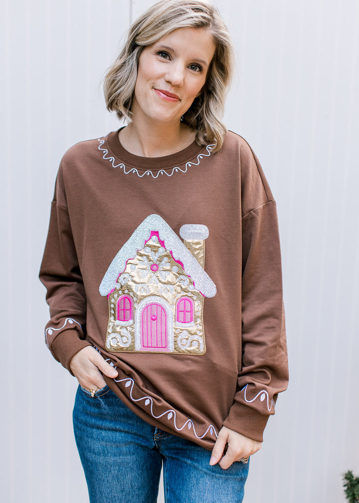 Brown Christmas pullover with gold gingerbread house, pink door and windows, white scalloped trim and long sleeves.