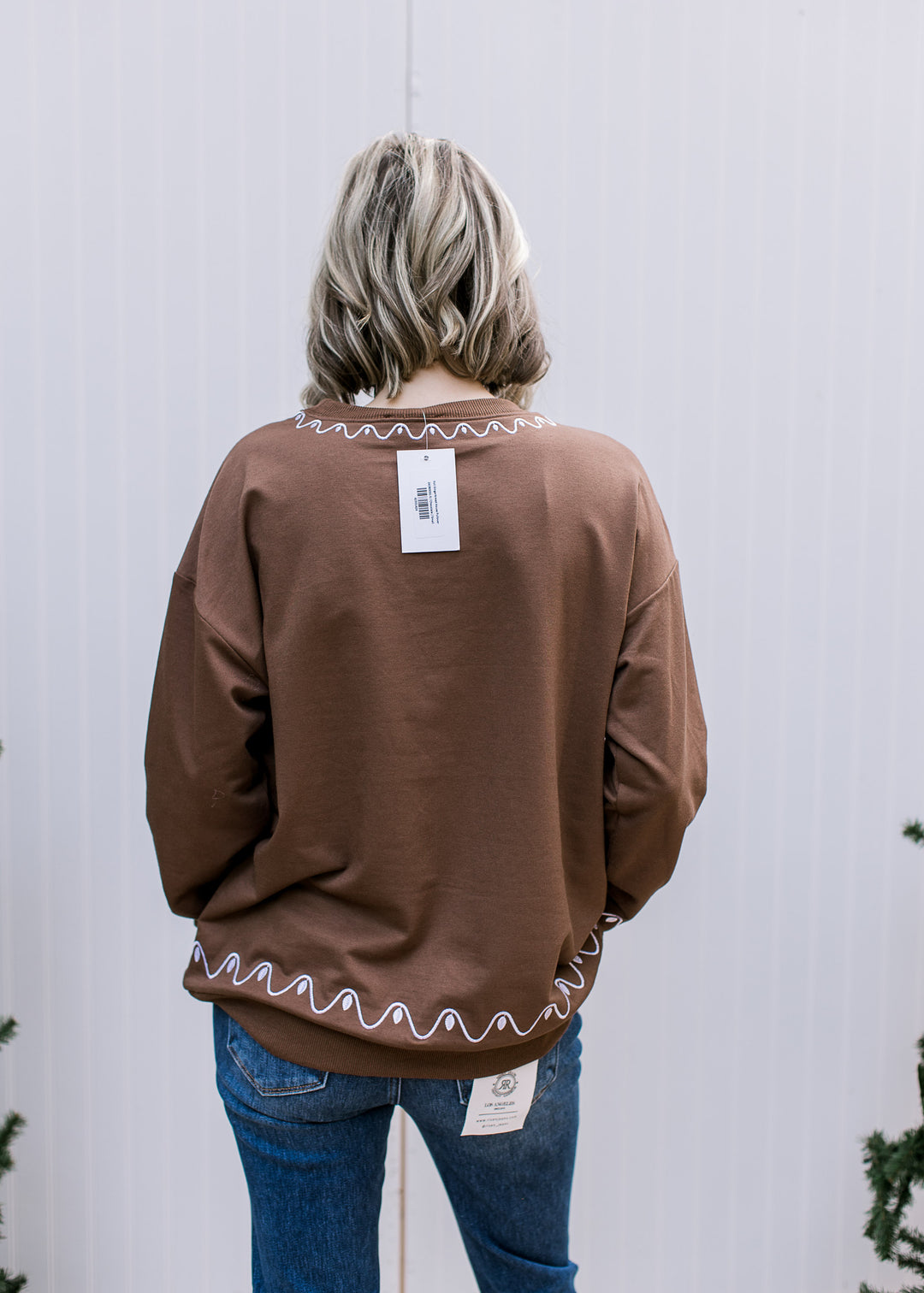 Back view of brown Gingerbread House Pullover with white scalloped stitching at neckline and hem, worn with jeans.