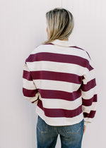 Back view of model wearing a burgundy and cream rugby stripe long sleeve top with cuffs.