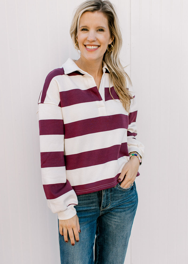 Model wearing a burgundy and cream rugby stripe long sleeve top with a v-neck and a collar.