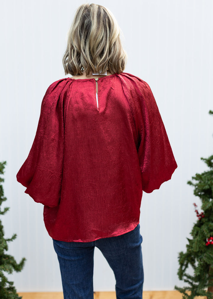 Back view of Burgundy Pleats Top showing buttoned keyhole neckline, shoulder pleats, bubble sleeves and loose hem.