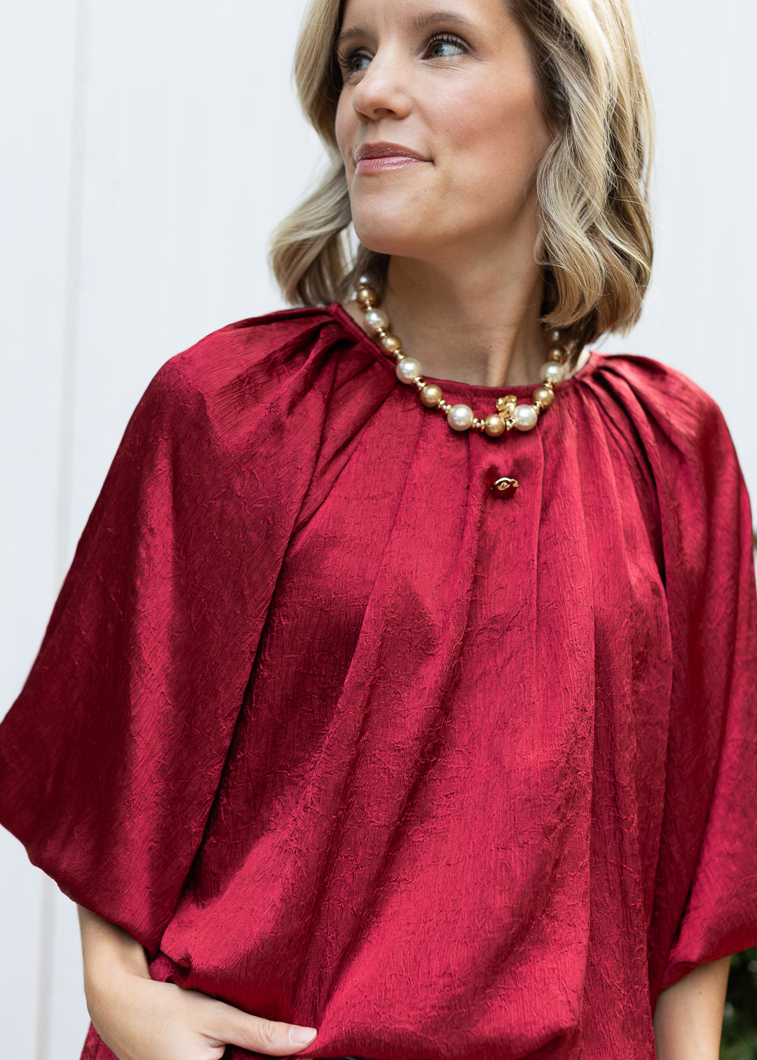 Close-up of Burgundy Pleats Top showing pleated round neckline, decorative gold buttons and lustrous textured fabric.