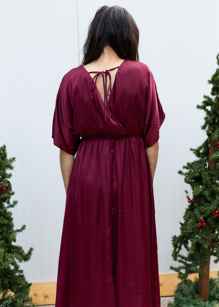 Back view of burgundy satin dress with V-back, delicate tie closure, gathered waist and elbow-length sleeves.