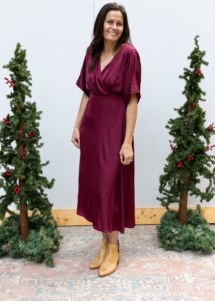 Burgundy satin midi dress with crossover V-neckline, elbow-length sleeves and flowing skirt, styled with tan boots.