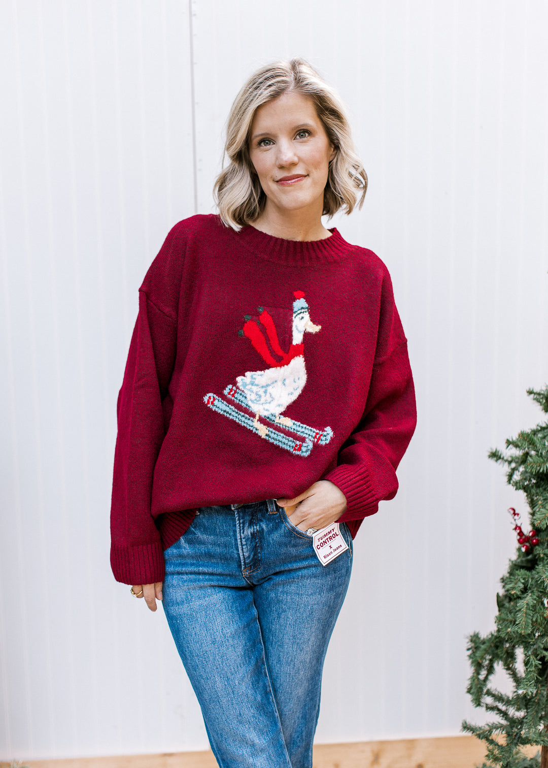 Burgundy Skiing Goose Sweater styled with blue jeans, showing relaxed fit, dropped shoulders and ribbed cuffs.