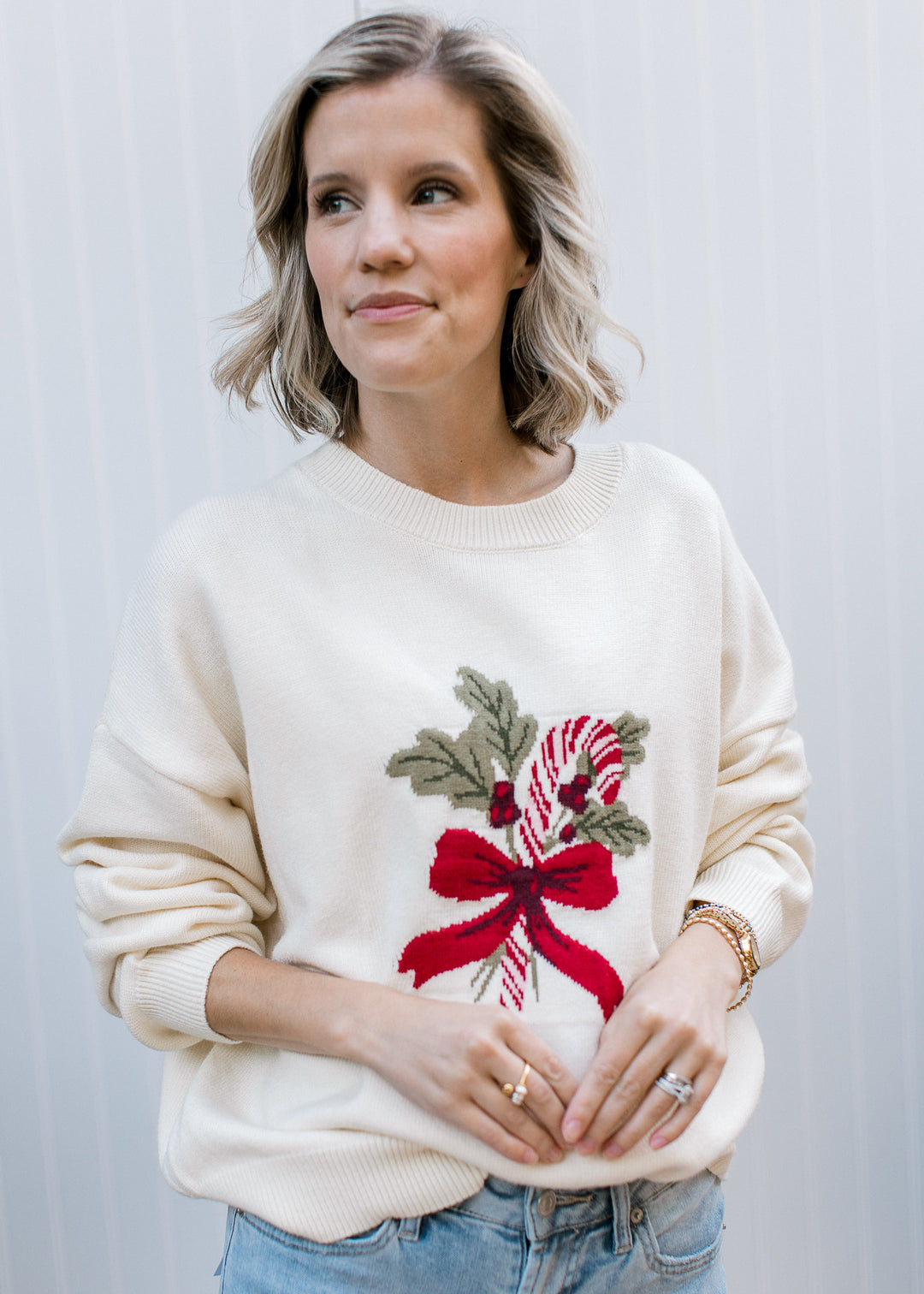 Front view of cream Candy Cane and Holly Sweater with ribbed crew neck and long sleeves, styled with light blue jeans.