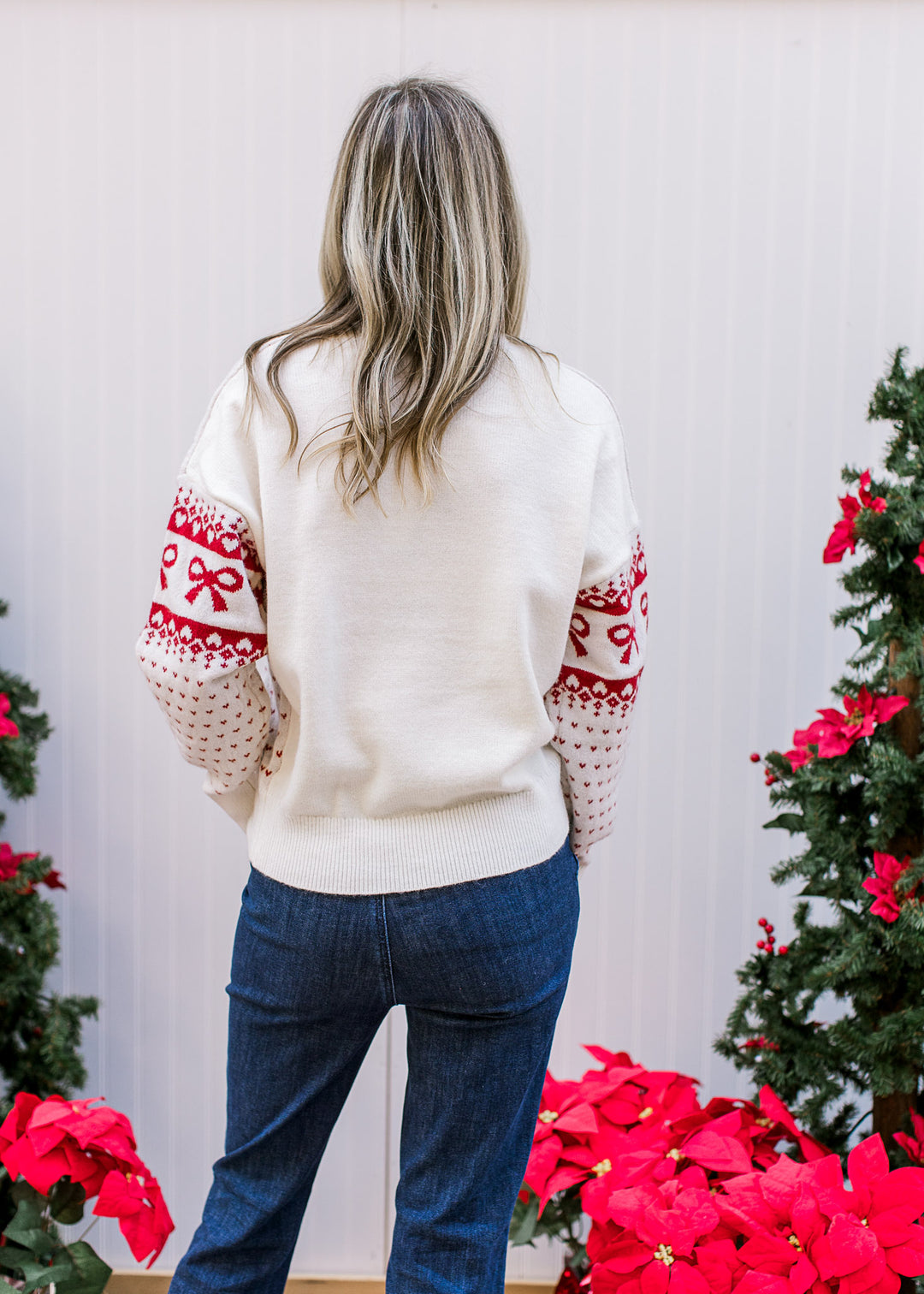 Back view of model wearing a cream slightly cropped sweater with red bow and heart accents. 