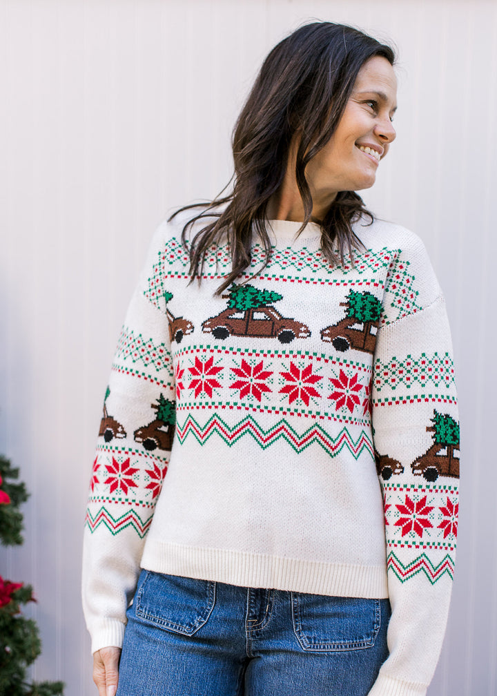 Model wearing a cream sweater with a round neck, long sleeves and brown trucks carrying a tree.