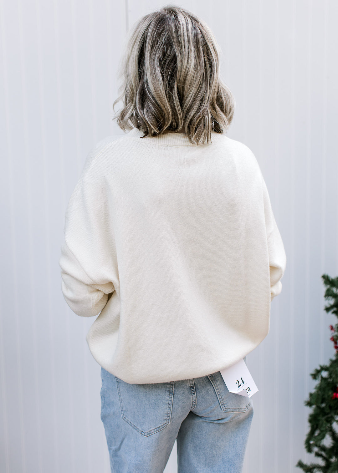 Back view of cream Candy Cane and Holly Sweater showing plain knit, relaxed fit and dropped shoulders over jeans.