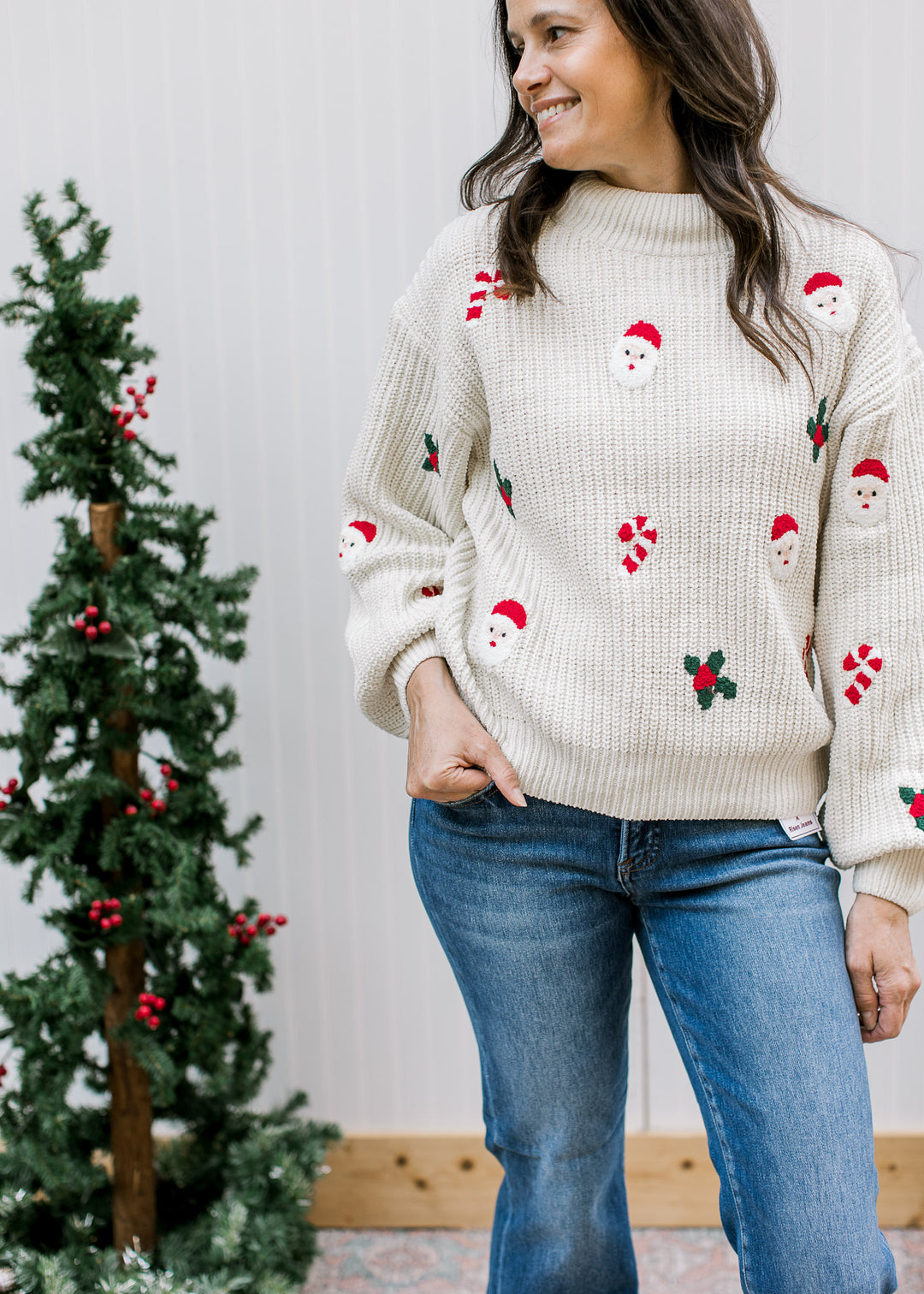 Cream Santa Christmas sweater with red candy canes, green holly, mock neck and long sleeves, shown with blue jeans.