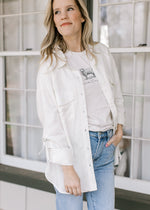 Model wearing a tee under a cream button down top with patch pockets and long sleeves.