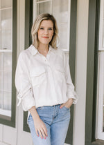 Model wearing a cream button down top with patch pockets and long sleeves with 3/4 clasp. 