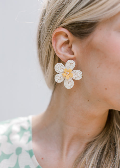 Model wearing  straw daisy earrings with  yellow and pearl details.