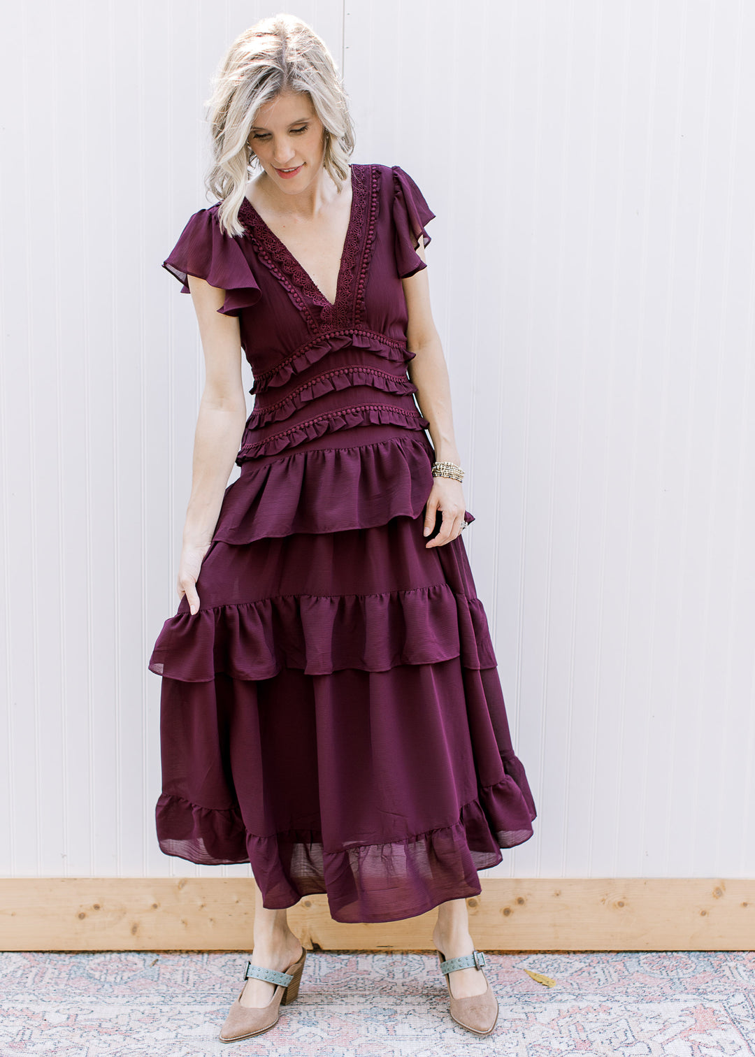 Model looking down in dark wine midi dress, showing layered flutter sleeves, lace bodice and gathered ruffle skirt.