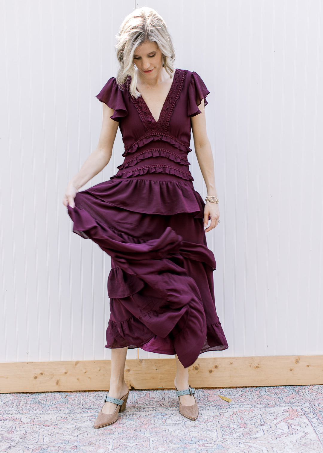 Model holding out one side of dark wine midi dress, displaying cascading ruffles and lace-trimmed V-neckline.
