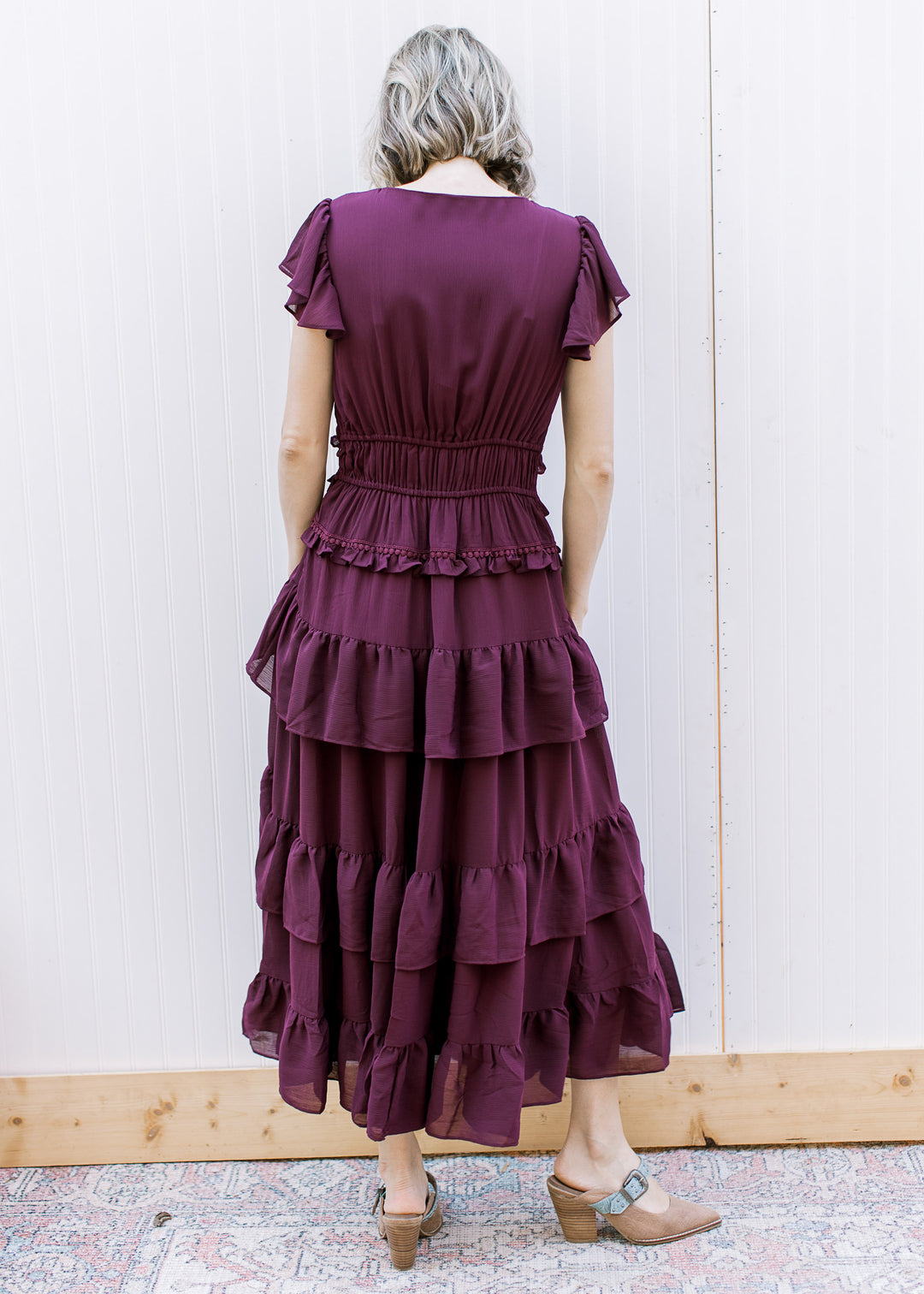 Back view of dark wine midi dress with elastic waist, flutter sleeves, round neckline and layered skirt ruffles.