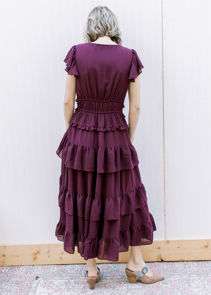 Back view of dark wine midi dress with elastic waist, flutter sleeves, round neckline and layered skirt ruffles.