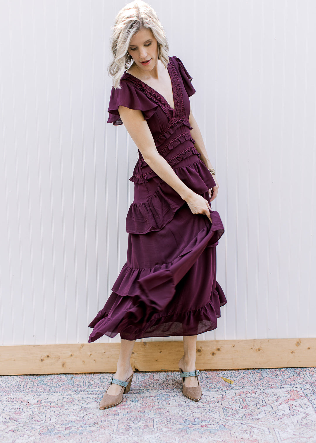 Side angle of dark wine ruffle dress with model lifting the skirt, showing layered tiers and a sheer hem.