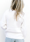 Back view of Model wearing a white lightweight knit sweater with a flag pattern and long sleeves.
