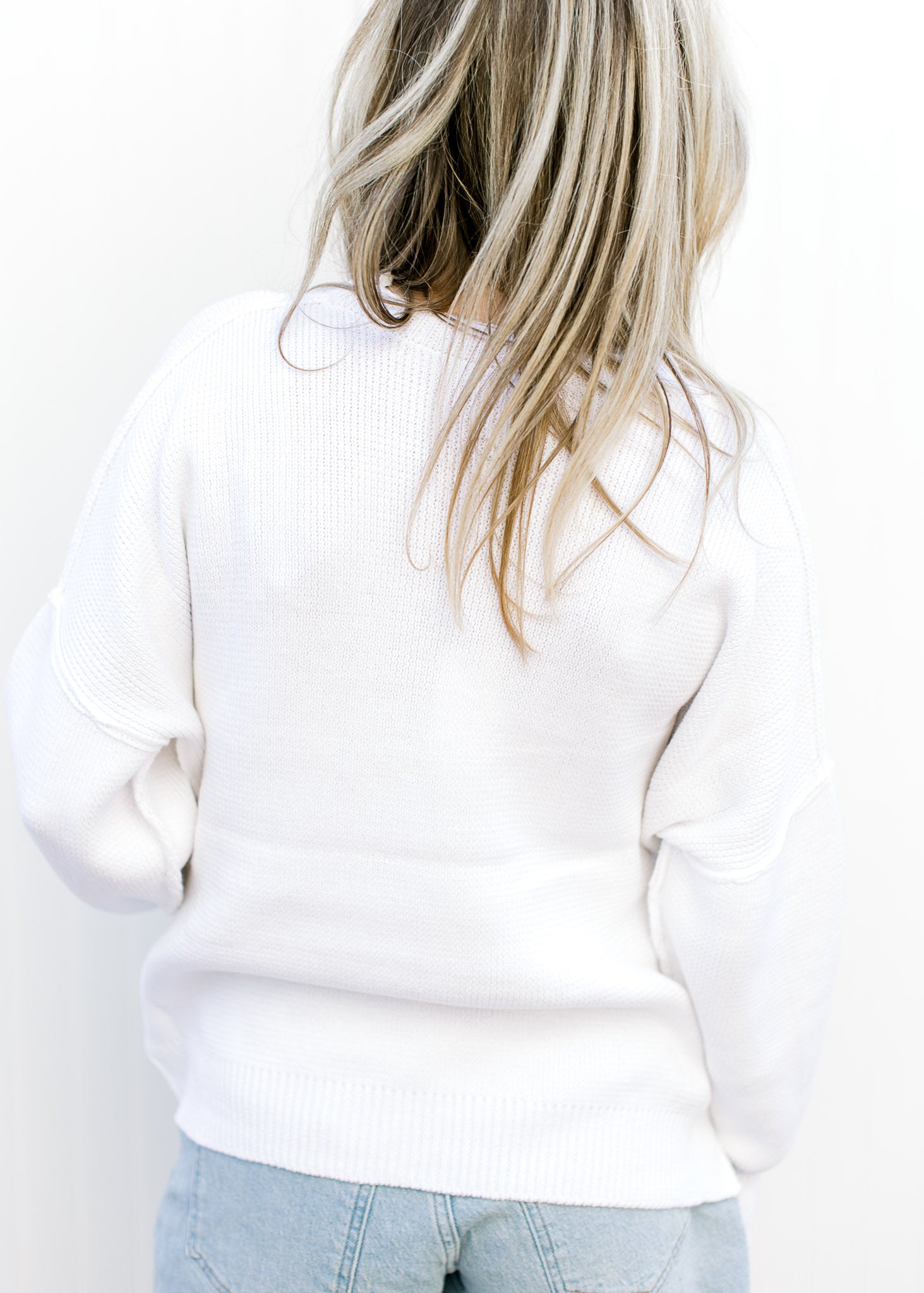 Back view of Model wearing a white lightweight knit sweater with a flag pattern and long sleeves.