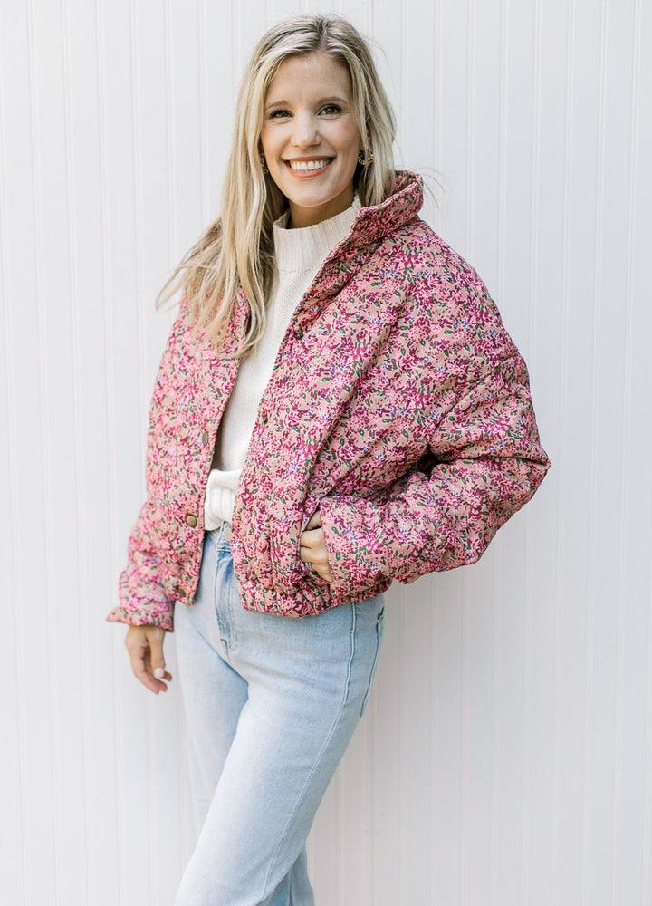 Model wearing a rose puffer jacket with pink flowers, long sleeves and pockets. 