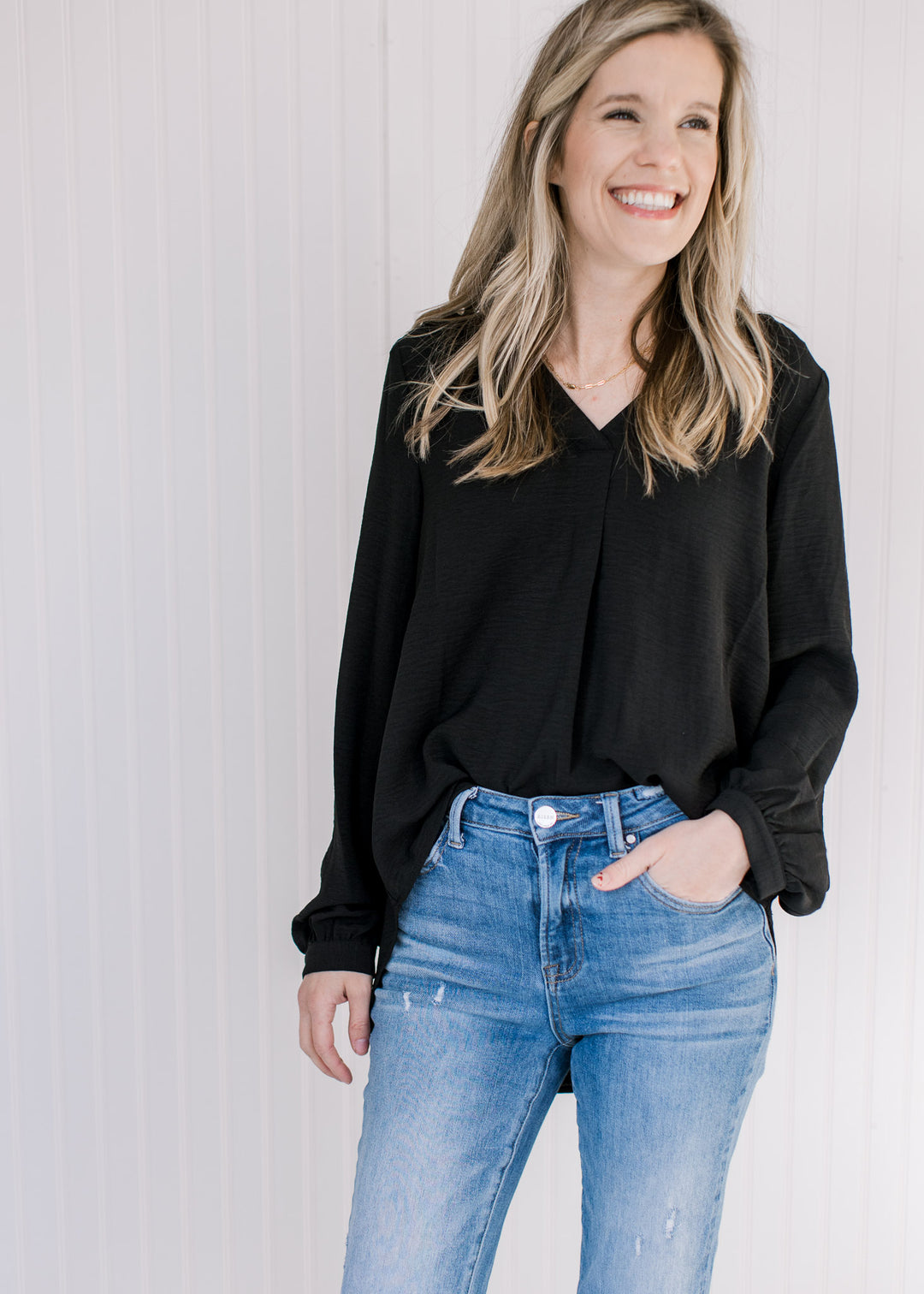 Model wearing a lightweight black v-neck top with button cuffs on the long sleeves. 