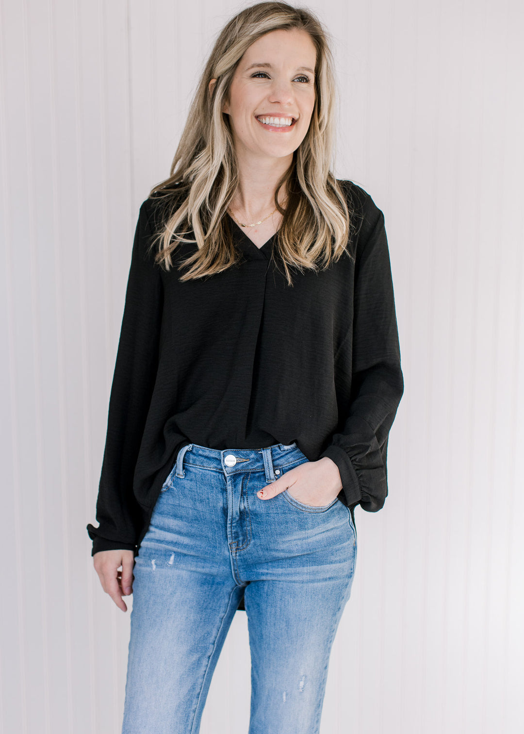 Model wearing a lightweight black v-neck top with long sleeves and button cuffs. 