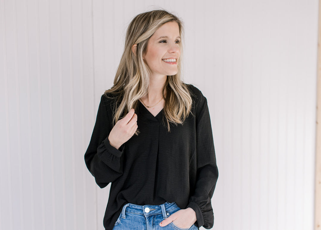 Model wearing a black v-neck top with long sleeves tucked into jeans. 