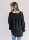 Back view of Model wearing a lightweight black v-neck top with button cuffs on the long sleeves.