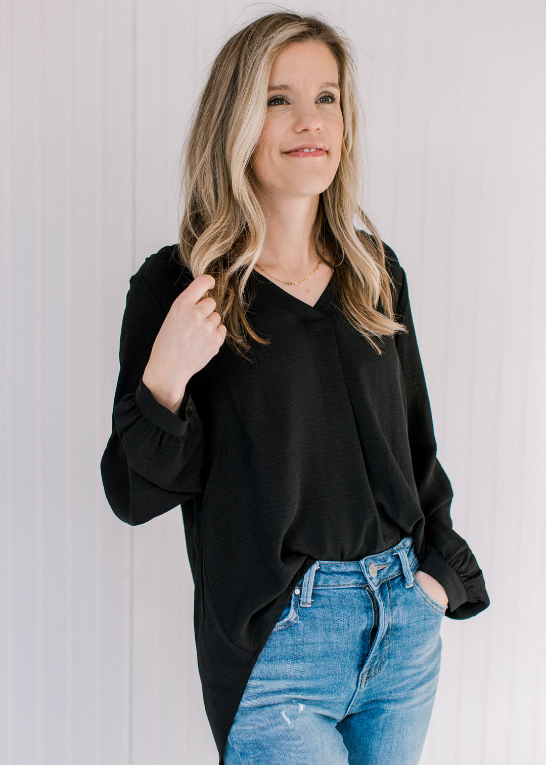 Model wearing jeans with a lightweight black v-neck top with button cuffs on the long sleeves.