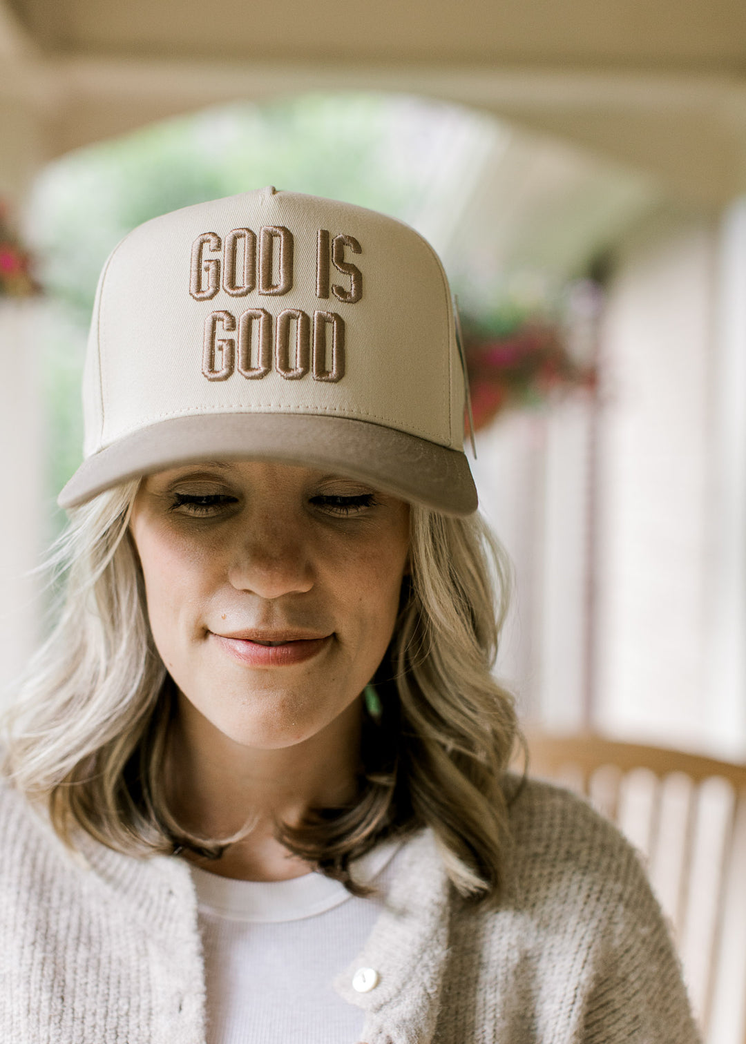 Model wearing a cream baseball cap with taupe bill and “God is Good” embroidered across the front.
