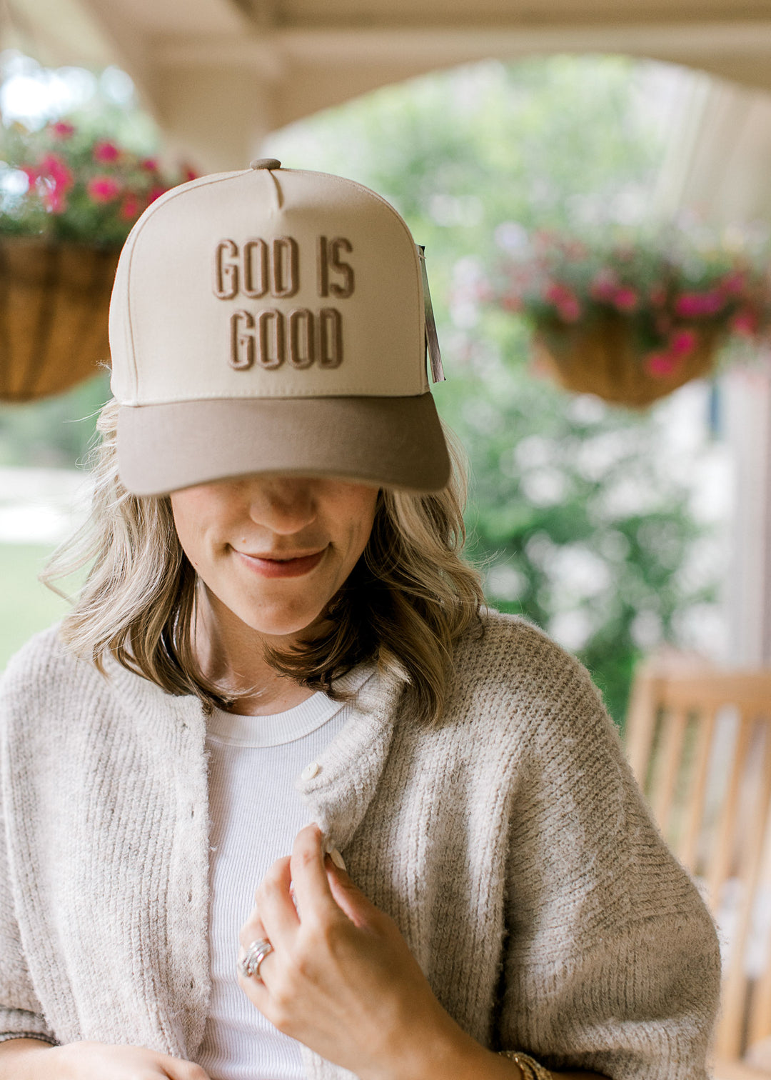 Model wearing a cream baseball cap with taupe bill and button with “God is Good” on front.