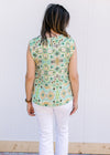 Back view of Model wearing white sleeveless top with green and gold pattern and single button back.