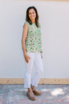 Model wearing white jeans with a white sleeveless top with green and gold ikat pattern. 