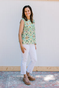 Model wearing white jeans with a white sleeveless top with green and gold ikat pattern. 