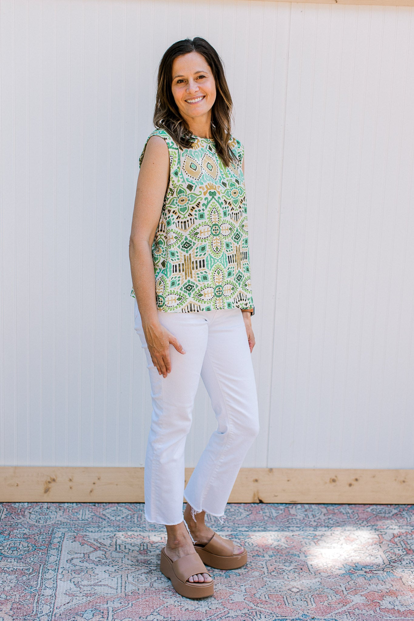 Model wearing white jeans with a white sleeveless top with green and gold ikat pattern. 