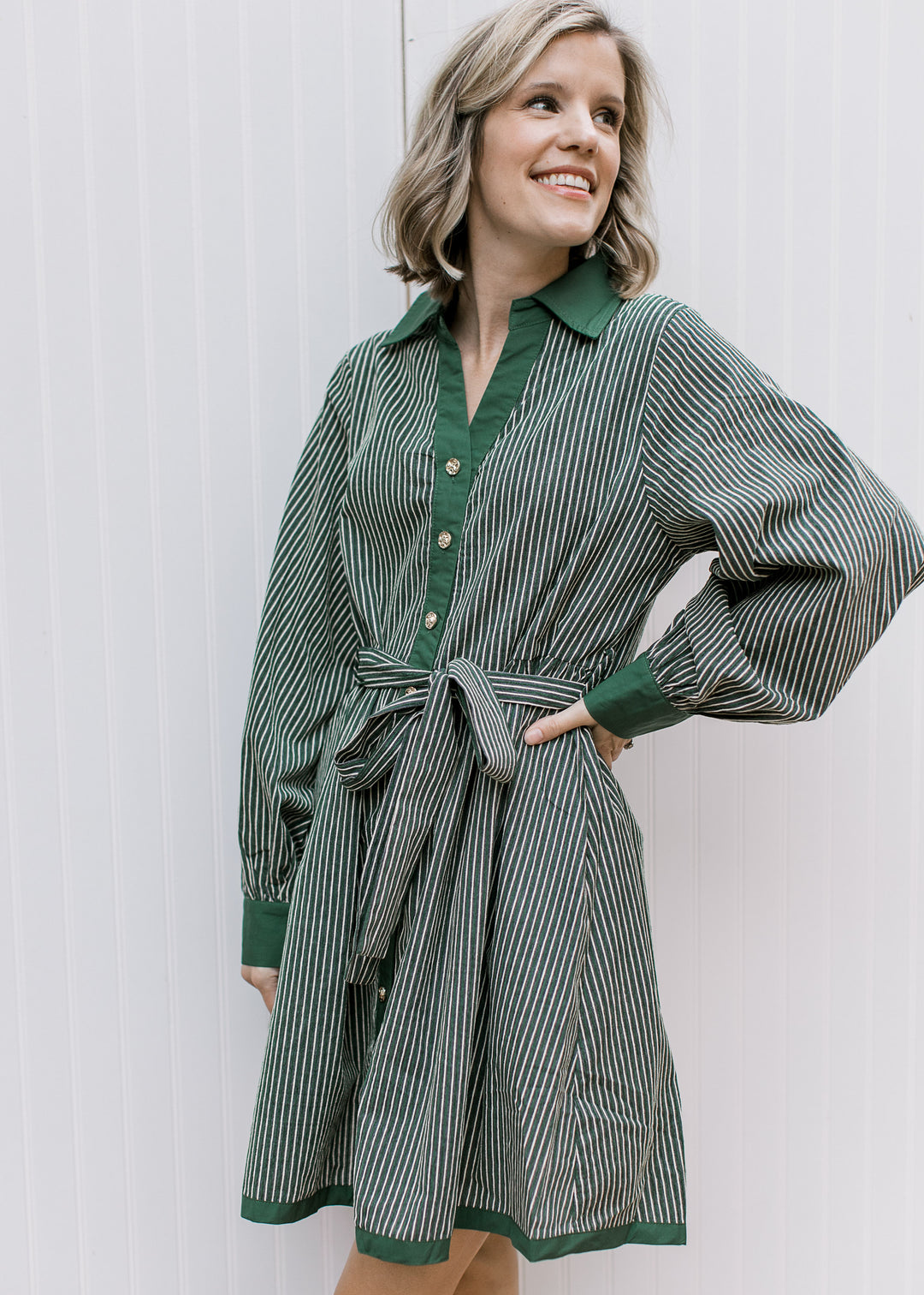 Front view of green and cream striped dress with tie waist, gold buttons, long gathered sleeves and solid green trim.