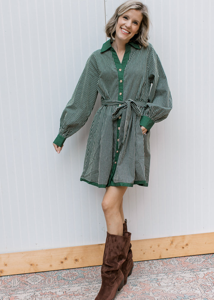 Model wearing green striped knee-length shirt dress with tie waist and side pocket, styled with brown tall boots.