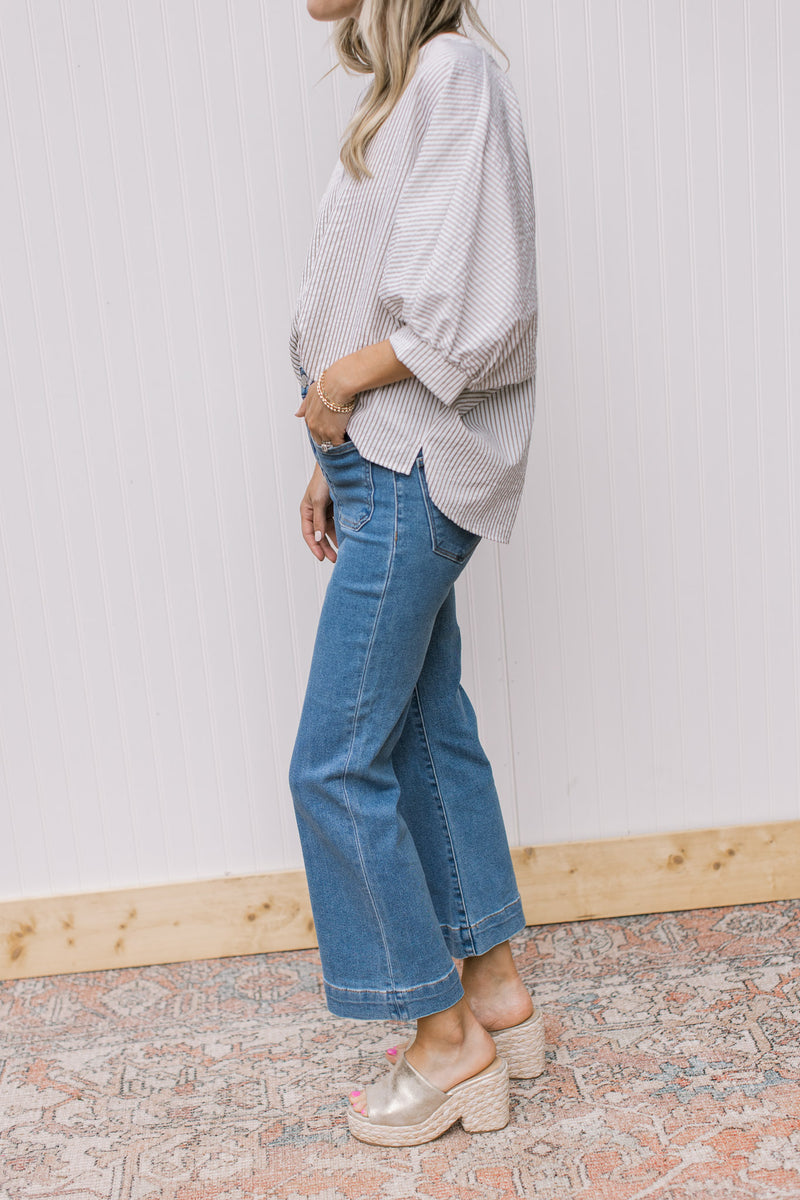 Side view of Model wearing medium washed jeans with front patch pockets and ankle boot cut.