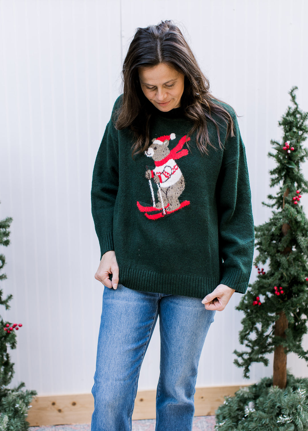 Front view of hunter green Skiing Bear Sweater with red skis, long sleeves and ribbed hem, worn loose over blue jeans.