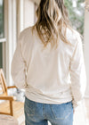 Back view of Model wearing a cream long sleeve tee with black script “and now I’m found”.