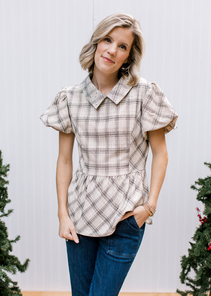 Model wearing jeweled collar plaid top with bubble sleeves and flared peplum hem, styled with dark blue jeans.