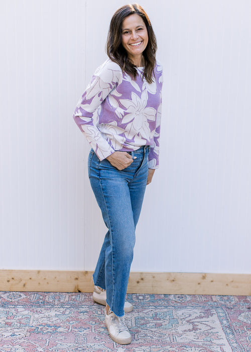 Model wearing a lavender long sleeve sweater with cream flowers and metallic details. 