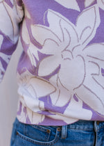 Close up of metallic detail and cream flowers on a lavender sweater with long sleeves. 