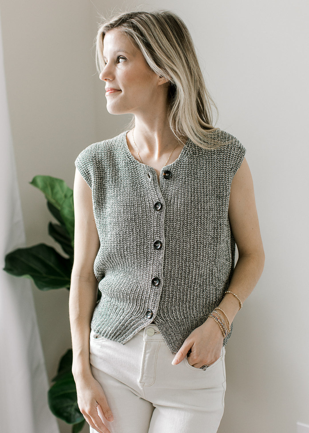 Model wearing white pants and a black and white marled cap sleeve sweater with a button front. 