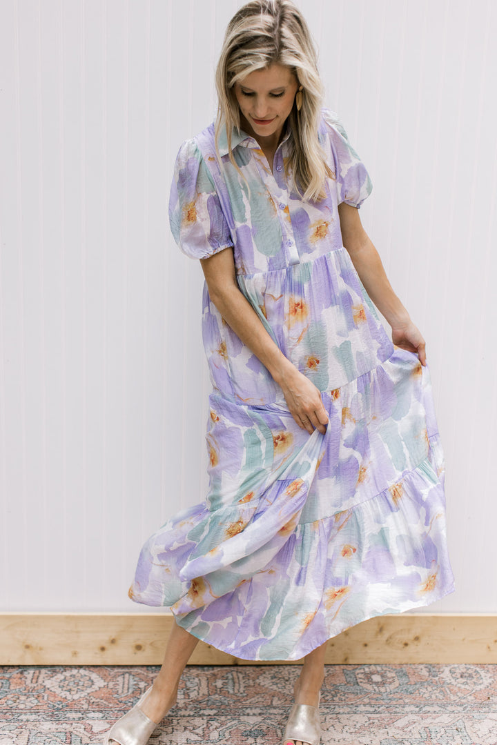 Model wearing a cream dress with lavender and aqua watercolor, bubble short sleeves and buttons. 