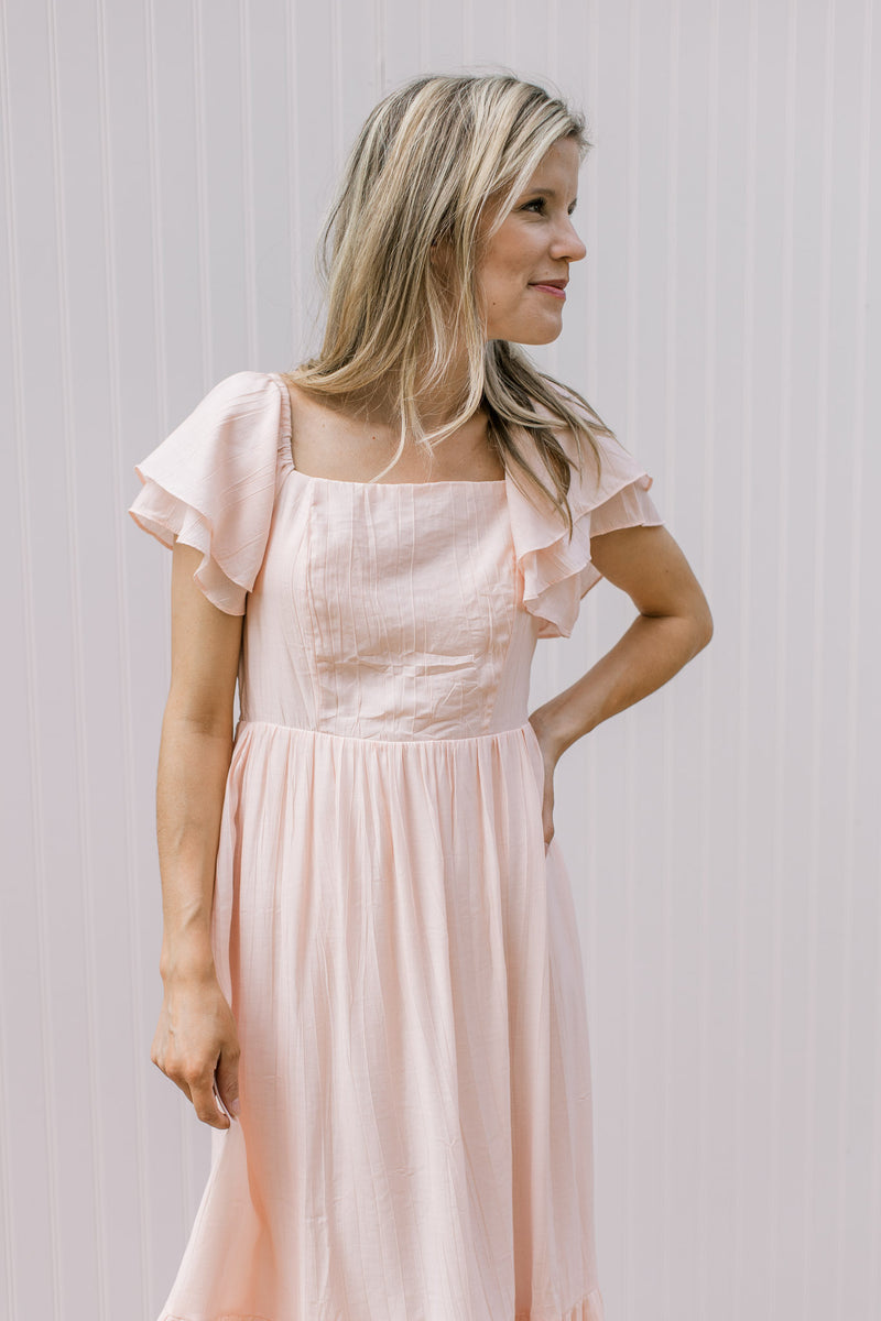 Model wearing a soft blush midi with layered ruffled sleeves and a square neck.
