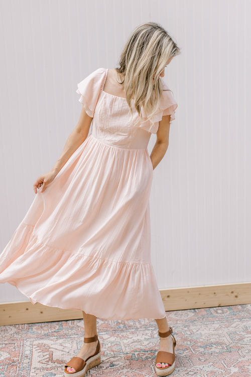 Model wearing wedges with a soft blush midi with layered ruffled sleeves and a square neck.
