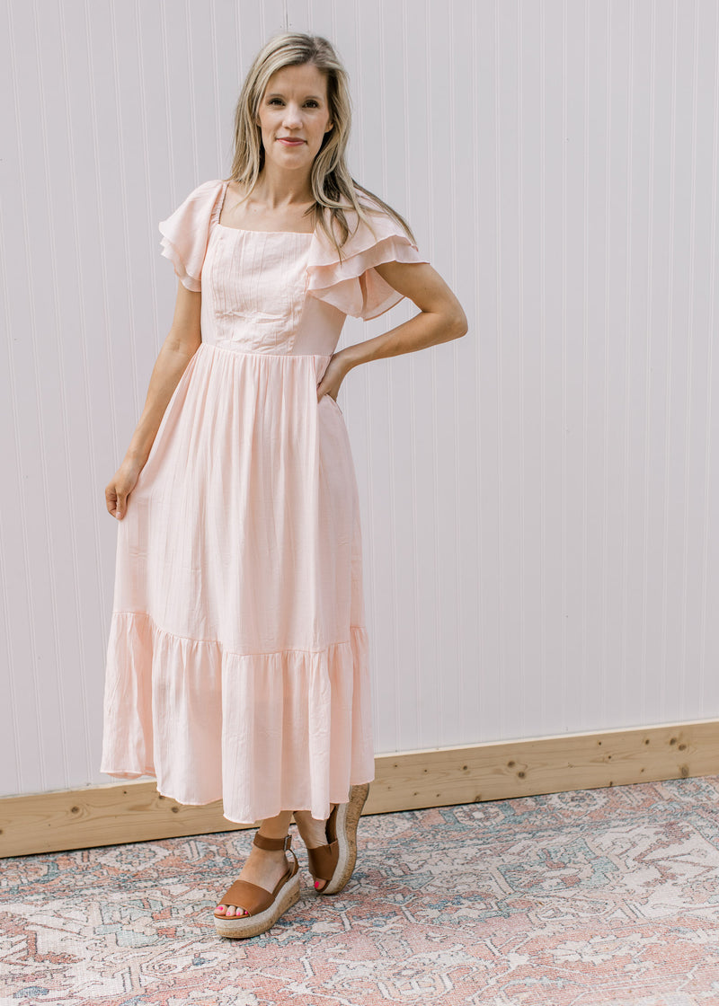 Model wearing a flowy blush midi with layered ruffled sleeves and a square neck.